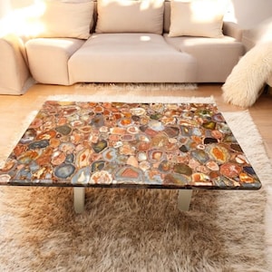 May include: A coffee table with a unique agate stone top. The top is made of many different colors and shapes of agate, creating a beautiful and natural pattern. The table has a simple, modern design with silver legs.