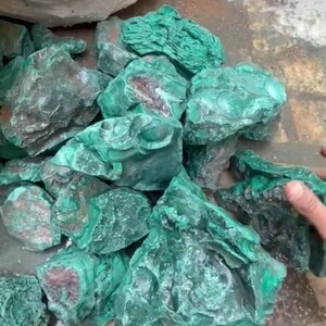 May include: A pile of rough, green malachite stones. The stones are various sizes and shapes, with some showing a darker green color.
