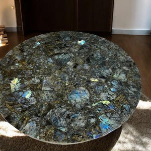 May include: A round table top made of labradorite stone. The stone is a dark gray with blue and green iridescent flecks.