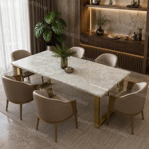 Può includere: Un moderno set da pranzo con un tavolo rettangolare in marmo bianco con gambe color oro, circondato da sei sedie imbottite beige. La stanza ha una palette di colori neutri con accenti in legno e una grande finestra.