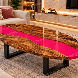 Könnte beinhalten: Ein ovaler Couchtisch mit einer Oberfläche aus Naturholzmaserung mit glänzendem Finish und einer breiten, leuchtend pinkfarbenen Harzeinlage, die durch die Mitte verläuft. Der Tisch wird von zwei stabilen, U-förmigen schwarzen Metallbeinen getragen.