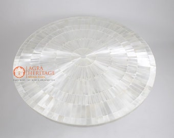 May include: A round, white decorative table top with a radial pattern. The surface is made of small, rectangular pieces arranged in concentric circles, creating a textured, mosaic-like appearance. The table top is from Agra Heritage Marble Crafts.