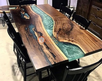 Puede incluir: Mesa de comedor rectangular de madera con un río de resina turquesa en el centro. Seis sillas negras rodean la mesa. La madera presenta un patrón de vetas natural. La mesa mide unos 200 cm de largo.