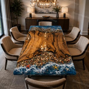Pode incluir: Uma mesa de jantar retangular com um design único. A mesa apresenta um centro de madeira com uma borda de resina que imita uma cena de praia, completa com seixos, estrelas do mar e ondas do oceano. A mesa é rodeada por cadeiras estofadas bege.