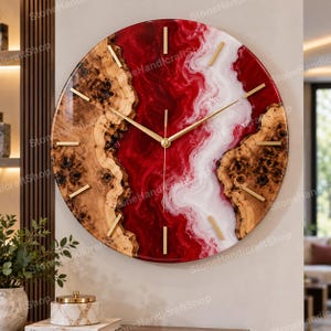 May include: A round wall clock featuring a natural wood burl edge with a glossy resin center in swirling shades of deep red and white. The clock face includes thin gold-toned metal hour markers and matching gold-toned hands at the center.