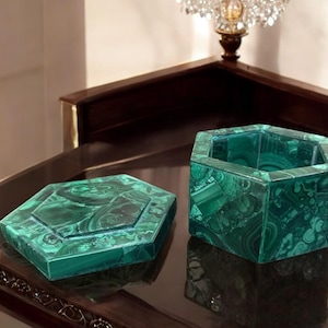 May include: A pair of hexagonal malachite boxes, one with a lid, sit on a dark, reflective surface. The boxes are a vibrant green with swirling patterns, showcasing the natural beauty of the stone. The open box reveals its interior.