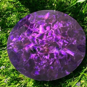 Könnte beinhalten: Ein runder, violetter Amethyst-Untersetzer mit einer polierten, glänzenden Oberfläche. Der Untersetzer besteht aus vielen kleinen Amethyststücken, die miteinander verklebt wurden.