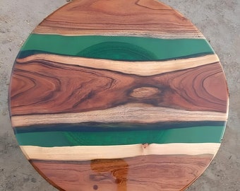 May include: Circular wooden table featuring a dark brown wood grain. A green epoxy resin band is set into the centre. The table's surface is smooth and polished, highlighting the natural wood patterns. The table would measure approximately 76 cm in diameter.