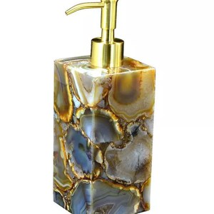 May include: A gold pump soap dispenser with a square base made of agate. The agate is a mix of brown, gray, and white with a swirling pattern.