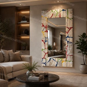 May include: A large rectangular mirror with a colorful, mosaic-like frame. The frame features a mix of white, red, blue, yellow, and green pieces. The mirror reflects a living room with a beige sofa and a round coffee table.