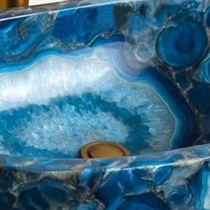May include: An oval-shaped, blue stone sink with a polished finish. The sink features a striking pattern of swirling blue and white colors, with a central drain. The sink's design resembles natural agate stone, adding a touch of elegance to any bathroom.