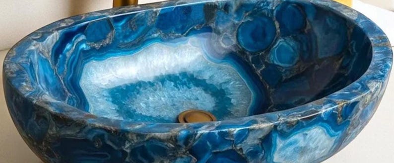 May include: An oval-shaped, blue stone sink with a polished finish. The sink features a striking pattern of swirling blue and white colors, with a central drain. The sink's design resembles natural agate stone, adding a touch of elegance to any bathroom.