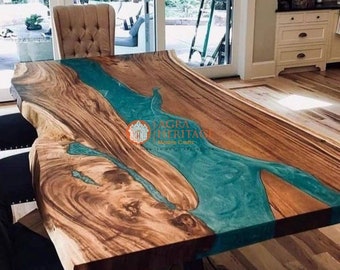 Puede incluir: Una mesa de comedor de madera con borde natural que presenta un diseño de río central hecho de resina turquesa translúcida. La madera muestra un patrón de veta natural con tonos marrones. El texto AGRA HERITAGE Marble Crafts está impreso en el centro.