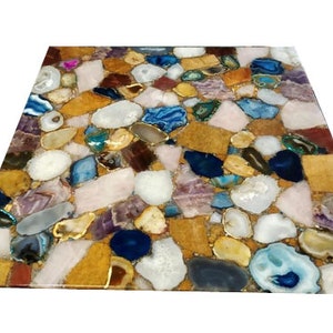 May include: A square, mosaic-style tabletop featuring a vibrant arrangement of polished gemstones. The surface showcases a mix of colors, including white, blue, gold, brown, and purple, creating a unique and decorative design. The gemstones are set in a clear resin.