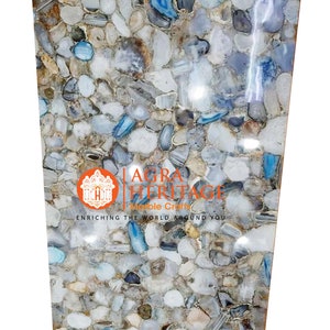 May include: A rectangular stone slab with a mosaic pattern of various-sized, polished stones in shades of white, gray, and blue. The surface has a glossy finish. The text "AGRA HERITAGE Marble Craft" is visible.