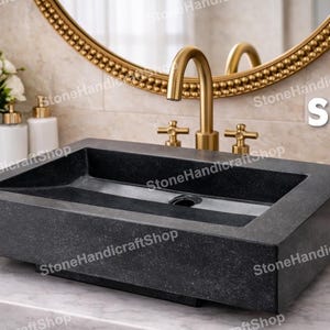 May include: A rectangular, dark gray stone sink with a sloped design. The sink is positioned on a marble countertop, with a gold faucet and mirror in the background. The text "Style 1" is visible.