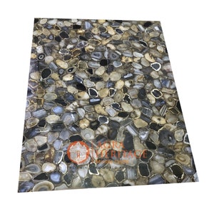 May include: A rectangular stone slab with a mosaic pattern of irregularly shaped, polished stones in shades of gray, black, and beige, with gold-colored accents. The slab has the text "AGRA HERITAGE" and "ENRICHING THE WORLD AROUND YOU".