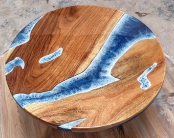 May include: A circular table top made from natural brown wood with a prominent grain pattern, featuring a decorative inlay of translucent blue resin that flows across the surface in a river-like design with white foamy accents along the edges.