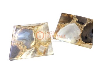 May include: Two irregularly shaped, polished stone coasters. The coasters feature a mix of gray, white, and gold tones, with a translucent quality. The text "AGRA HERITAGE" is visible on the coasters. These coasters are ideal for home decor.