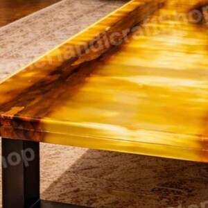 May include: A close-up of a rectangular table with a glossy, amber-colored surface. The table has dark brown veining and a black metal base. The table is likely made of onyx or a similar material.