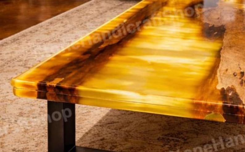 May include: A close-up of a rectangular table with a glossy, amber-colored surface. The table has dark brown veining and a black metal base. The table is likely made of onyx or a similar material.