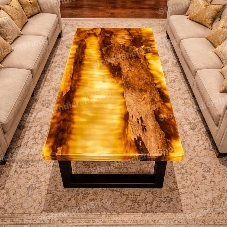 May include: A rectangular coffee table with a unique design. The tabletop features a translucent, amber-colored resin with embedded wood grain. The table is supported by a black, rectangular metal frame. The table is surrounded by beige sofas.