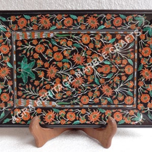 Puede incluir: Una bandeja rectangular de mármol negro con un intrincado diseño floral incrustado con flores naranjas y hojas verdes. La superficie muestra el texto AGRA HERITAGE MARBLE CRAFTS en letras blancas en el centro del patrón floral.