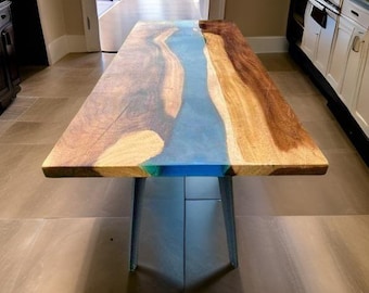 Può includere: Un tavolo in legno fatto a mano con un centro in resina epossidica blu a forma di fiume. Il tavolo presenta venature naturali del legno sui lati ed è sostenuto da gambe in metallo. Il tavolo è lungo circa 183 cm.