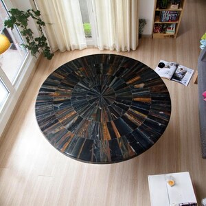 May include: A round table with a black and brown tiger eye stone mosaic top. The table is in a room with a wooden floor and white curtains.
