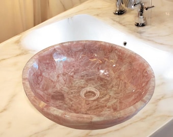 Pode incluir: Uma pia de banheiro de quartzo rosa com uma bancada de mármore branco. A pia é feita de pedra natural e tem um formato único e orgânico.