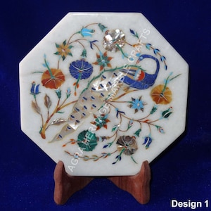 Può includere: Piatto ottagonale in marmo bianco con un design di pavone intarsiato con pietre colorate e madreperla. Il piatto è su un supporto in legno. Design 1.