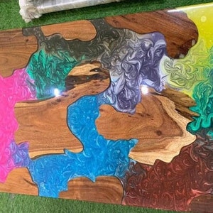 May include: A rectangular wooden table with a colorful epoxy resin design. The table features sections of natural wood grain interspersed with vibrant hues of pink, blue, green, yellow, and brown resin, creating a unique and artistic look.