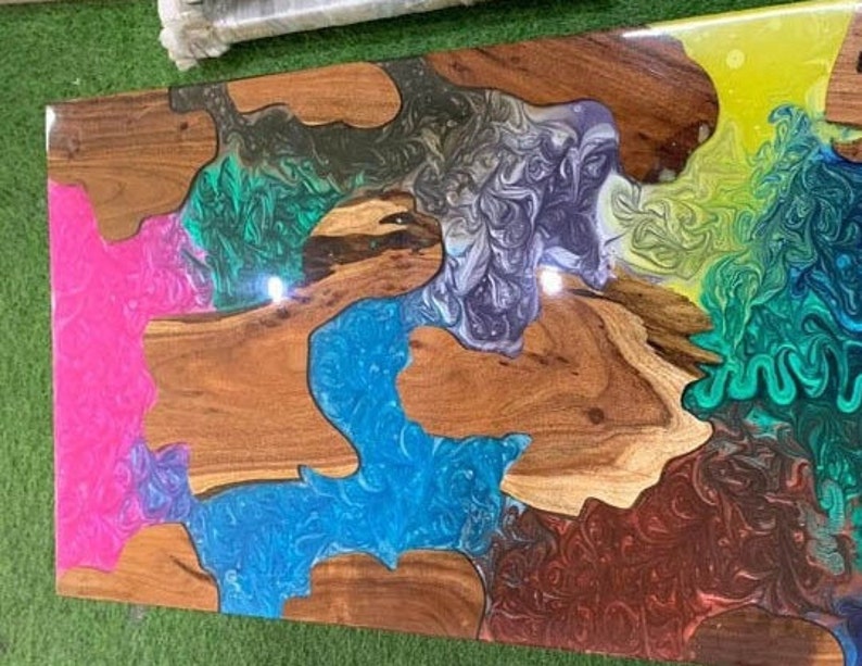 May include: A rectangular wooden table with a colorful epoxy resin design. The table features sections of natural wood grain interspersed with vibrant hues of pink, blue, green, yellow, and brown resin, creating a unique and artistic look.