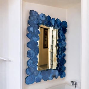 May include: A blue agate mirror with a unique, irregular frame. The mirror is rectangular and hangs on a white wall.