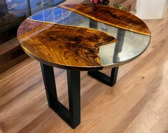 May include: Round wooden table with a clear epoxy resin top featuring a river-like design. The table has black metal legs.