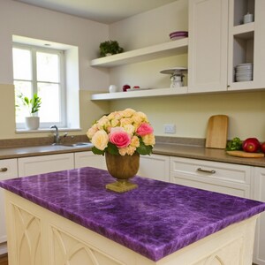 May include: A kitchen island with a vibrant purple countertop. A bouquet of pink and yellow roses sits in a wooden vase. White cabinets and shelves are visible in the background, creating a bright and inviting space.