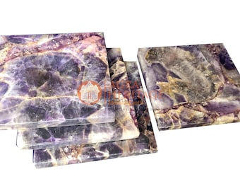 Puede incluir: Un conjunto de posavasos cuadrados de amatista. Los posavasos muestran una mezcla de tonos morados, blancos y grises, con una apariencia natural veteada. Los bordes son lisos y pulidos, mostrando los patrones únicos de la piedra.