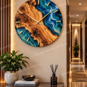 May include: A round wall clock featuring a natural wood grain center with a live edge design, contrasted by swirling blue and teal epoxy resin sections. The clock face includes gold-colored hour markers and thin gold-colored clock hands.