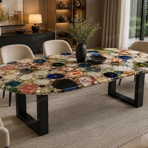 May include: An oval dining table featuring a polished surface composed of multicolored agate slices embedded in clear resin. The tabletop displays a mosaic of circular stone patterns in blue, red, green, and brown, supported by two black metal U-shaped legs.