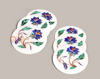 Puede incluir: Juego de seis posavasos de mármol blanco con un diseño floral. Cada posavasos presenta una rosa azul con hojas verdes y acentos rojos. Los posavasos están hechos de piedra incrustada y son perfectos para agregar un toque de elegancia a cualquier hogar.