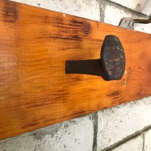 Op de afbeelding: Een rustiek houten plank met een grote, roestige spijker erin geslagen. De spijker dient als haak om items aan op te hangen.