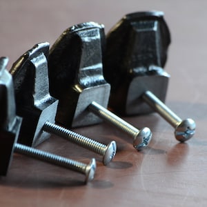May include: Four black metal cabinet knobs with silver screws. The knobs have a unique, slightly rounded, rectangular shape.