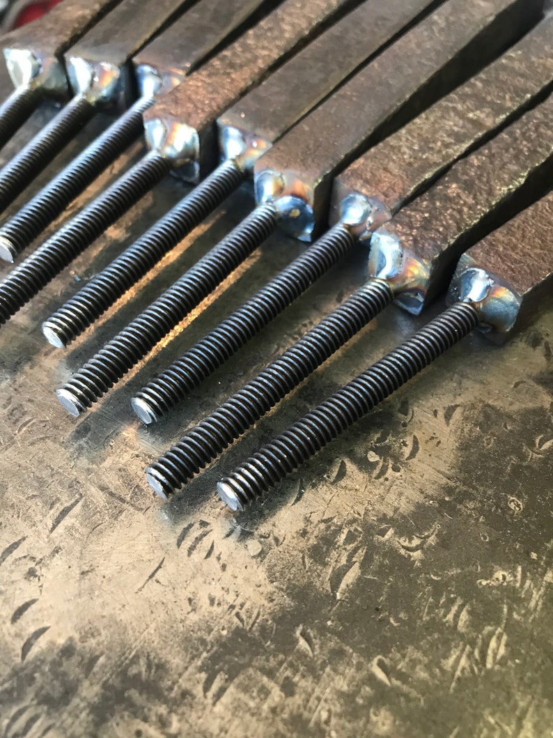 Op de afbeelding: Close-up van een groep metalen staven met schroefdraad aan de uiteinden. De staven zijn in een rij gerangschikt en zijn allemaal even groot. De uiteinden van de staven zijn vierkant gelast.