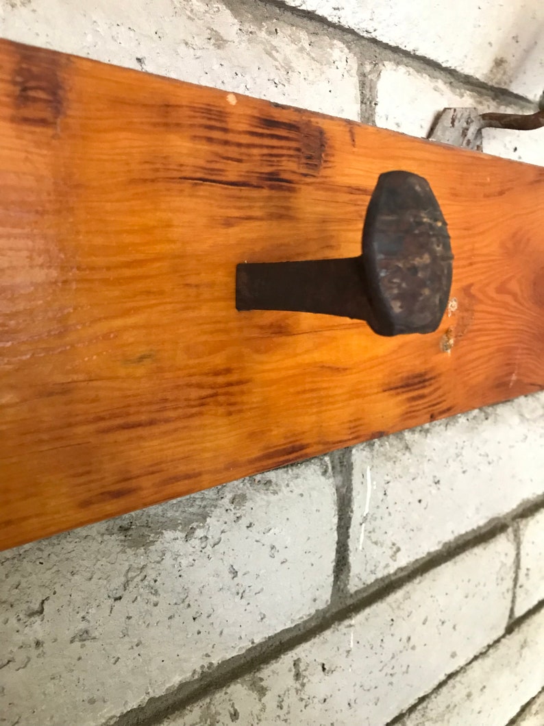 Op de afbeelding: Een rustiek houten plank met een grote, roestige spijker erin geslagen. De spijker dient als haak om items aan op te hangen.