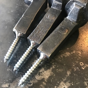 Op de afbeelding: Drie zwarte metalen haken met een schroefdraad. De haken zijn gemaakt van gesmeed metaal en hebben een rustieke uitstraling.