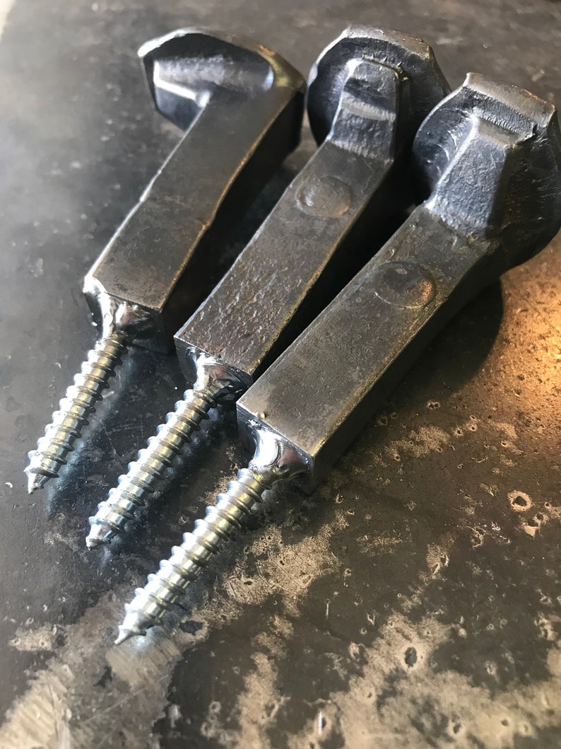 Op de afbeelding: Drie zwarte metalen haken met een schroefdraad. De haken zijn gemaakt van gesmeed metaal en hebben een rustieke uitstraling.