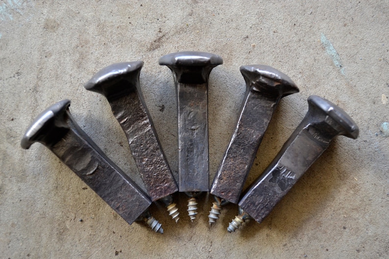 Op de afbeelding: Vijf antieke spoorwegspikes met schroefbevestigingen. De spikes zijn van metaal en hebben een donkergrijze afwerking. De schroefbevestigingen zijn van metaal en hebben een zilveren afwerking.