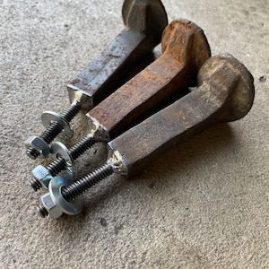 Op de afbeelding: Drie roestige metalen spoorwegspikes met vierkante koppen en schroefdraad aan de uiteinden. Elke spike is bevestigd aan een zilveren moer en ring.