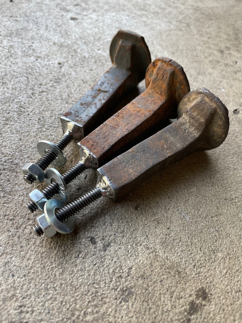 Op de afbeelding: Drie roestige metalen spoorwegspikes met vierkante koppen en schroefdraad aan de uiteinden. Elke spike is bevestigd aan een zilveren moer en ring.