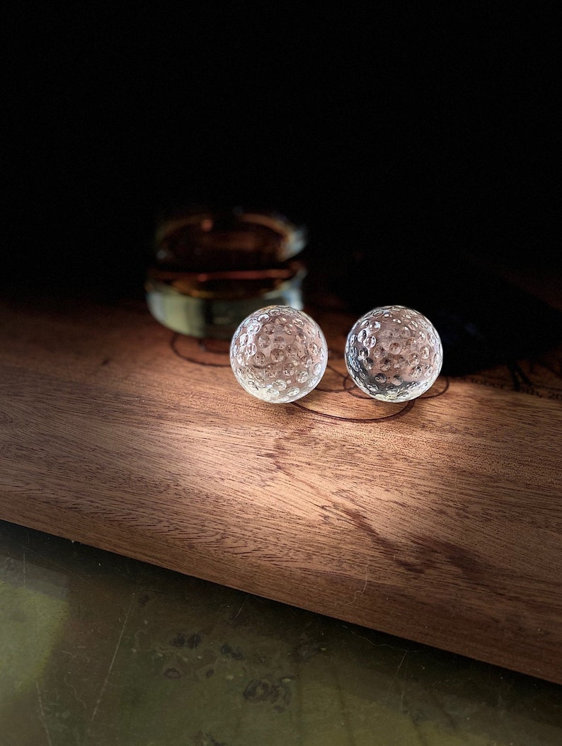 Op de afbeelding: Twee heldere glazen golfballen op een houten oppervlak.